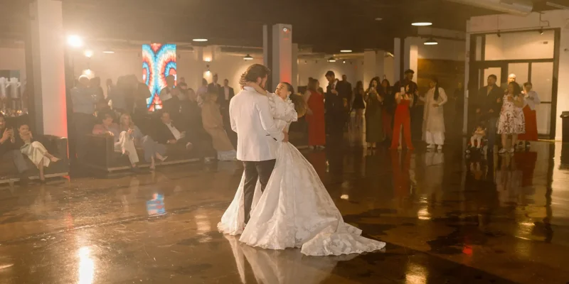 newly married couple dancing their first dance in the middle of a dimly lit reception hall, surrounded by cheering guests.